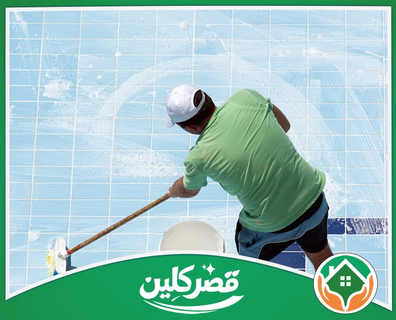 تنظيف مسابح فيبر جلاس بالرياض 0550575548 قصر كلين عامل ينظف أرضية مسبح زرقاء باستخدام ممسحة طويلة ورغوة صابون بيضاء، لضمان النظافة والتعقيم.