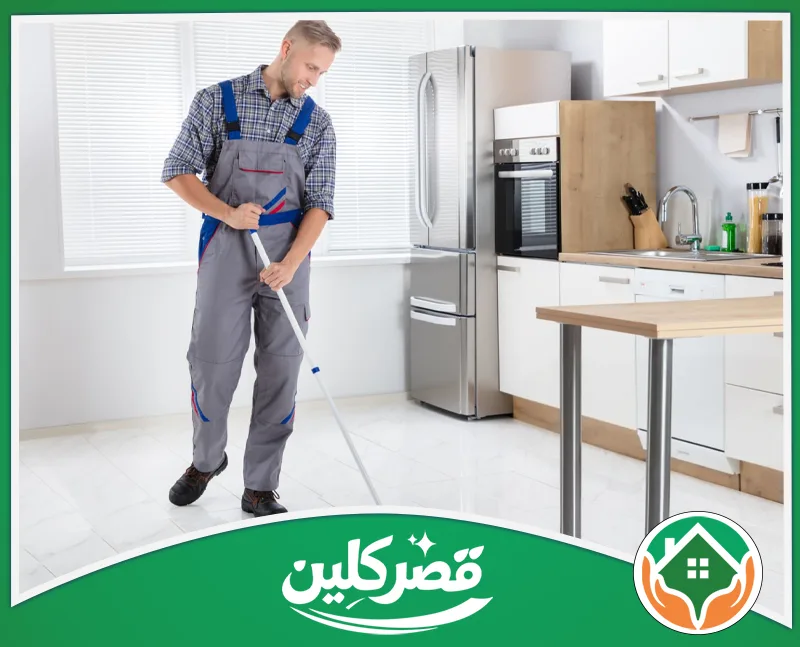 تنظيف مطابخ الألوميتال بالرياض 0550575548 قصر كلين عامل يرتدي زي العمل الرمادي ينظف ويلمع أرضية مطبخ حديث وأنيق باستخدام ممسحة يدوية بكل همة ونشاط.