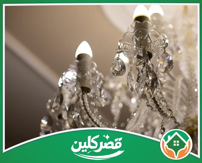 تنظيف نجف بالرياض 0550575548 قصر كلين قريبة لنجفة كريستال فاخرة، تتدلى منها قطع بلورية براقة تعكس إضاءة المصابيح الدافئة بجمال وأناقة
