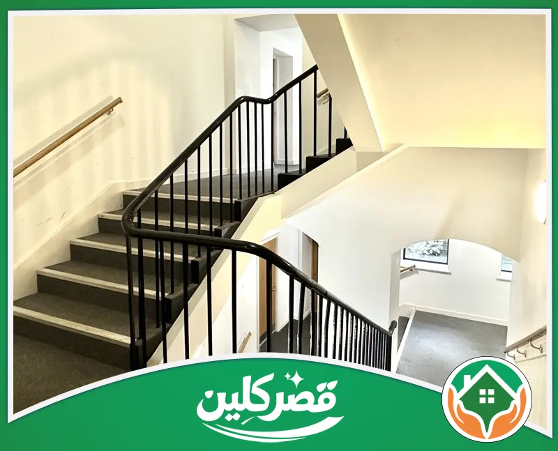 تنظيف عمائر تجارية بالرياض 0550575548 قصر كلين درج داخلي أنيق ومثالي مغطى بموكيت رمادي نظيف، يحيط به درابزين أسود وجدران بيضاء مبهجة تعكس الترتيب.