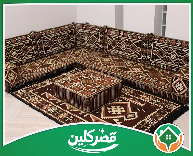 تنظيف أرضيات المجالس بالرياض 0550575548 قصر كلين جلسة أرضية تراثية باللون البني والبيج، بنقوش هندسية بدوية ساحرة، تشمل ديوانًا زاوياً، سجادة متناسقة، وطاولة مربعة.