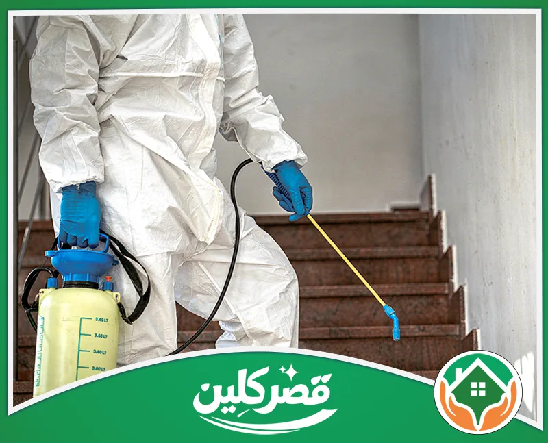 شركة مكافحة صراصير بالرياض 0550575548 قصركلين عامل ببدلة وقاية وقفازات زرقاء، يحمل مضخة يدوية ويرش درج مبنى داخلي بمبيدات الآفات أو التعقيم.