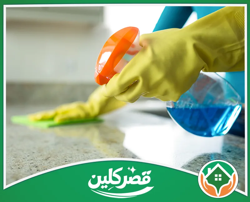 تنظيف وإزالة دهون المطابخ بالرياض 0550575548 قصر كلين تنظيف وتطهير الأسطح الرخامية باستخدام بخاخ منظف أزرق وقطعة قماش خضراء، ببراعة وأيدي ترتدي قفازات صفراء لحمايتها.