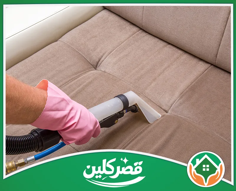 تنظيف كنب جلد بالرياض 0550575548 قصر كلين يد ترتدي قفازًا ورديًا تستخدم آلة شفط مخصصة لتنظيف وتطهير أريكة بيج، لتبدو منتعشة وخالية من الأتربة.