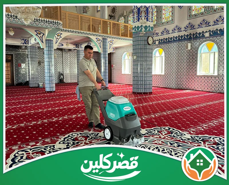 شركة تنظيف وتعقيم المساجد بالرياض 0550575548 قصر كلين تنظيف سجاد مسجد أحمر منقوش باستخدام ماكينة غسيل متطورة، داخل قاعة تتميز بأعمدة وجدران مزينة بالزخارف الإسلامية.