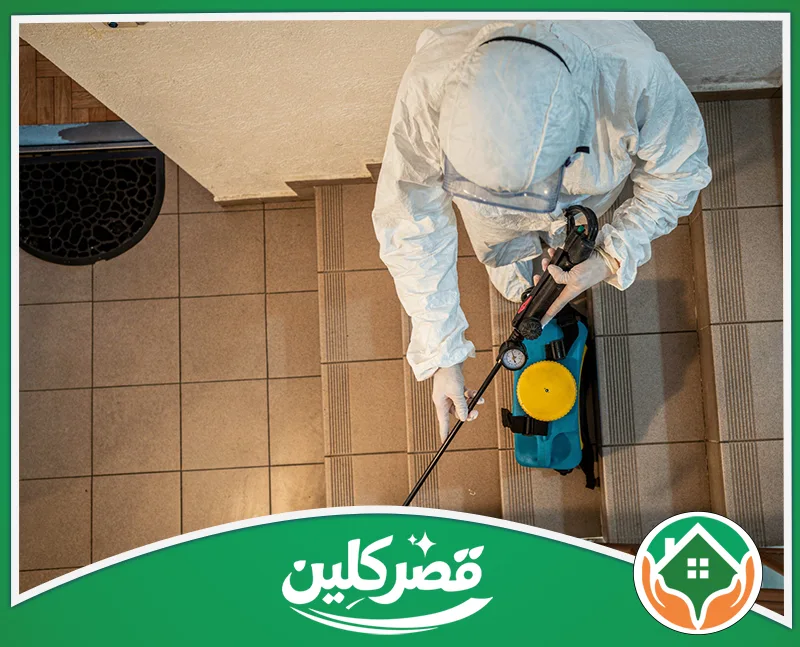 مكافحة حشرات المنازل بالرياض 0550575548 قصر كلين لقطة علوية لعامل يرتدي بدلة وقاية كاملة، يمسك بمرشة كيميائية أثناء تعقيم أو رش مبيدات على درج داخلي لمبنى.