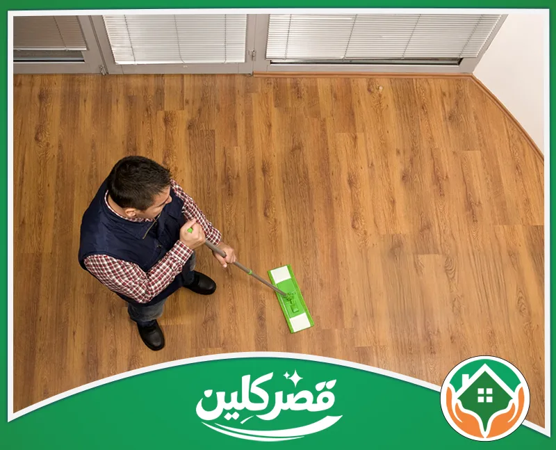 شركة تنظيف الكنب بالرياض 0550575548 قصر كلين رجل يستخدم ممسحة مسطحة خضراء لتنظيف وتلميع أرضية باركيه خشبية، لإعادة البريق والنظافة للمكان بعناية وإتقان.