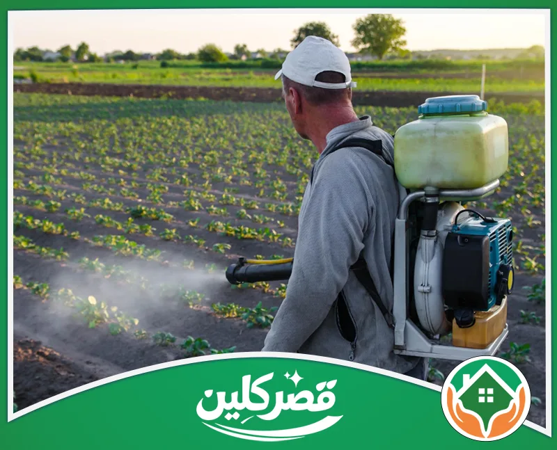 شركة مكافحة النمل الأبيض بالرياض 0550575548 قصر كلين مزارع يرتدي قبعة بيضاء ويحمل مضخة بمحرك على ظهره، يقوم برش مبيدات على المحاصيل الزراعية في الحقل.